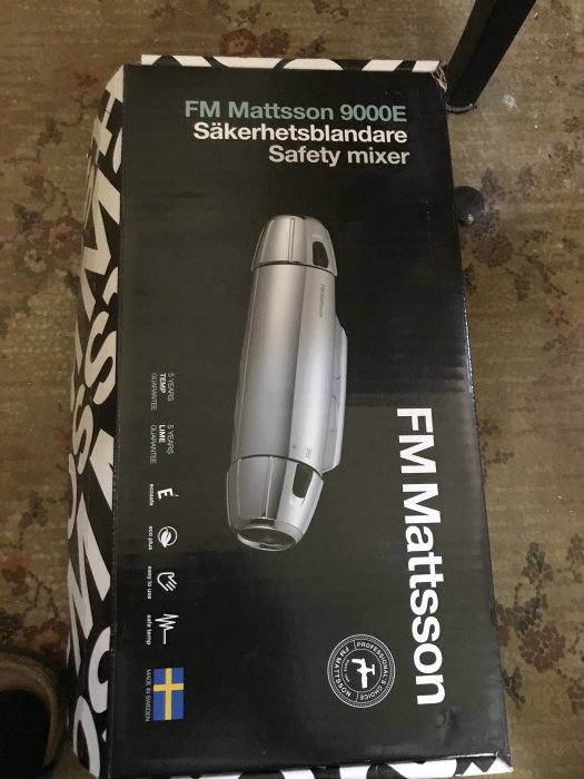 Oöppnad förpackning av FM Mattsson 9000E säkerhetsblandare på ett golv.