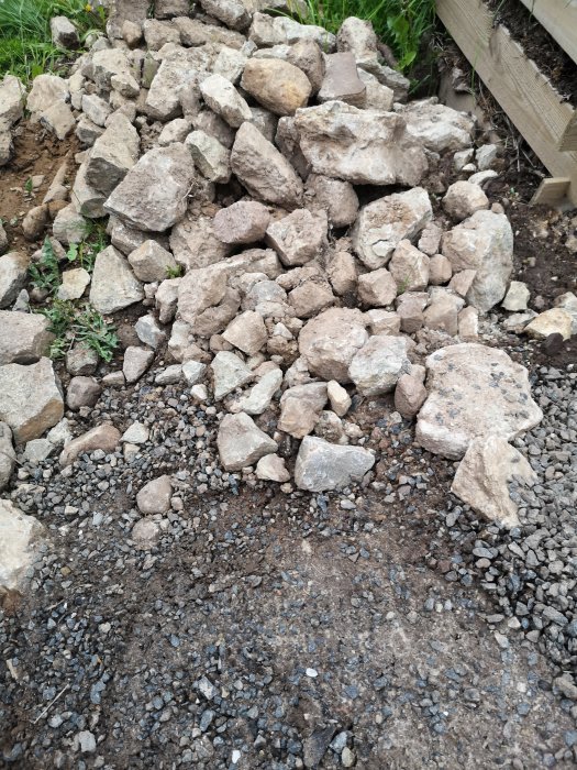 Ofärdig stödmur med blandning av stora och små stenar, några täckta med jord.