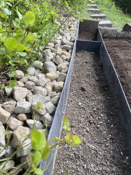 En nyanlagd smultronrabatt avgränsad av en dubbel plåtkant och stenar, med bar jord redo för plantering.