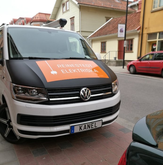 Vit Volkswagen transportbil med företagslogotyp och registreringsskylten 'KANEL' parkerad på gata.