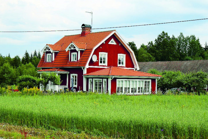 Rött traditionellt hus med stor utbyggnad och gräsremsa framför.