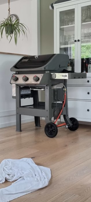 Närbild på en Weber Spirit 310 gasolgrill inomhus före användning, med en vit skyddsduk på trägolvet.