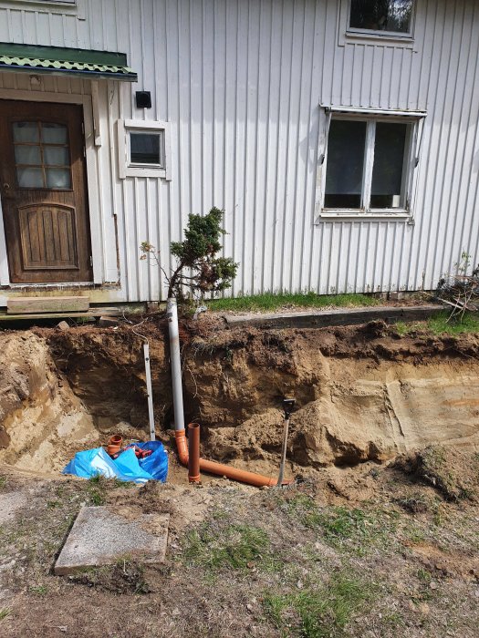 Uppgrävd framsida av hus med nyinstallerat avloppsrör och ansluten trekammarbrunn.