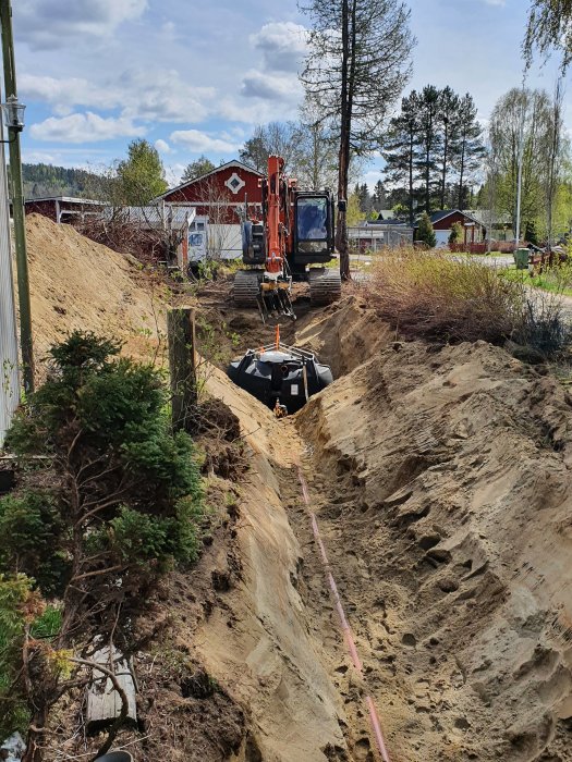 Grävmaskin vid uppgrävd framsida med nytt avloppsrör och ansluten trekammarbrunn.