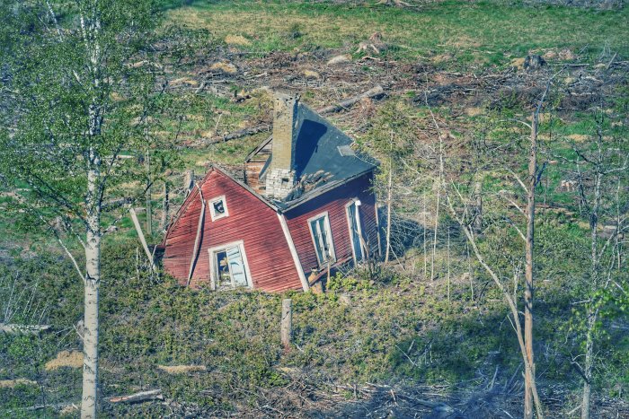 Rött övergivet hus som delvis kollapsat i skogsmiljö.