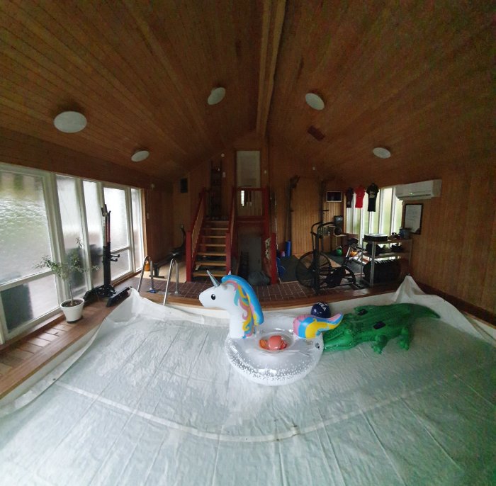 Inomhusvy av ett rum med takfönster, träpanel, träningsutrustning och uppblåsbara djurleksaker.