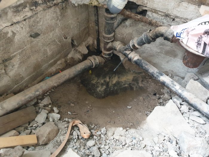 Gammal avloppsstam i järn och nylagt grundvatten i ett uppgrävt hål för bytt till plast och golvvärmeinstallation.