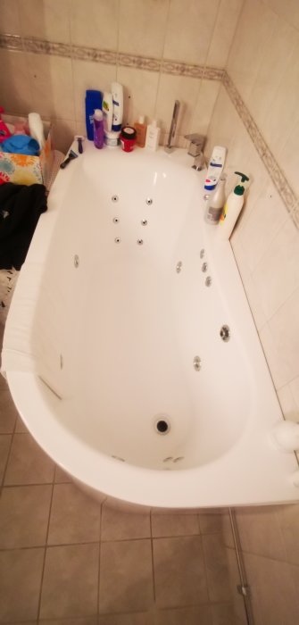 Vit hörnbadkar med jetmunstycken och hygienprodukter runt kanten.