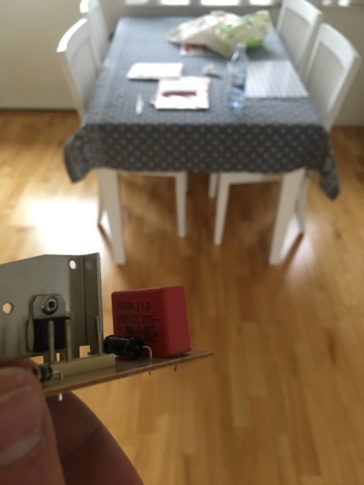 En person håller en kretskortsdel med en ny 1 µF röd kondensator för Siemensfrys, oskarp bakgrund.