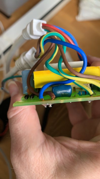 Närbild på hand som håller en kretskortsmodul med färgglada kablar och komponenter.