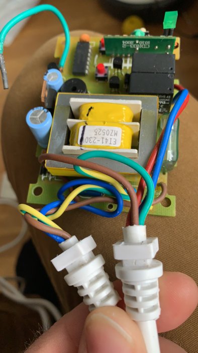 En hand håller en styrbox för projektorduk med synliga elektronikkomponenter och kopplingskablar.