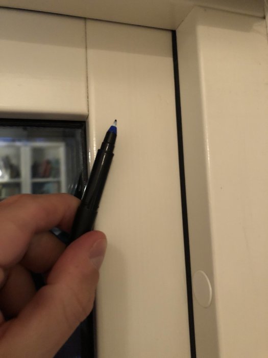 Hand håller en penna mot ovankanten av ett fönster för att illustrera placeringen av skruvar för kassettrullgardin.