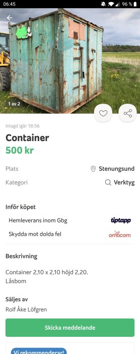 Sliten blå container med rost och skadad dörr på en gräsbevuxen mark.