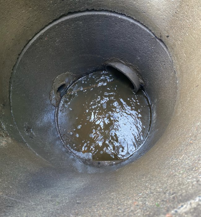 Närbild av ett översvämmat brunnsrör med inkommande vattenflöde.