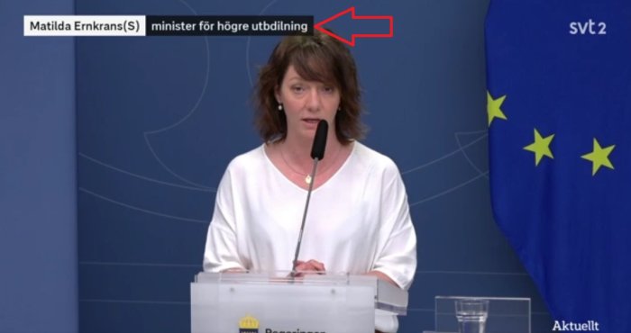 Kvinna talar vid podiet med feltextad undertext "minister för högre utbildining" på skärmen.