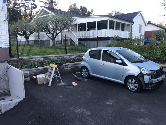 Nyinstallerat staket vid parkering med en liten bil i förgrunden, verktyg och stegar till vänster.