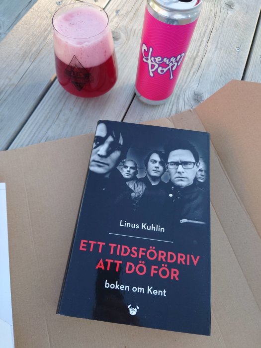 Bok om Kent med titeln "Ett tidsfördriv att dö för" på bord bredvid rosa dryck och burk.