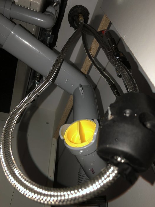 Vy under skåp med vattenrör och flexibla anslutningsslangar vid installation av kran.