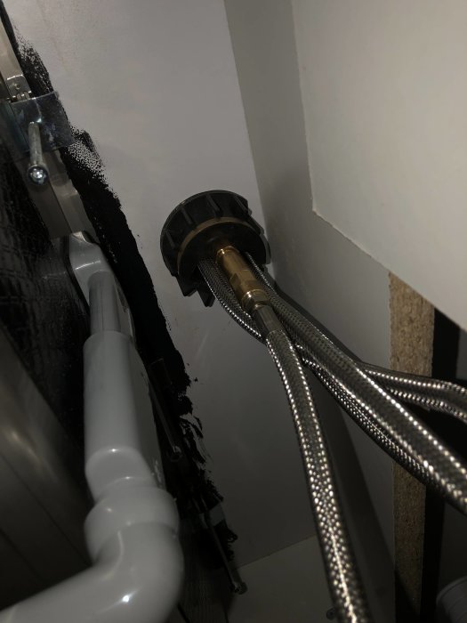 Utrymme under skåp med synliga vattenledningar och kopplingar som ska anslutas till en kran.