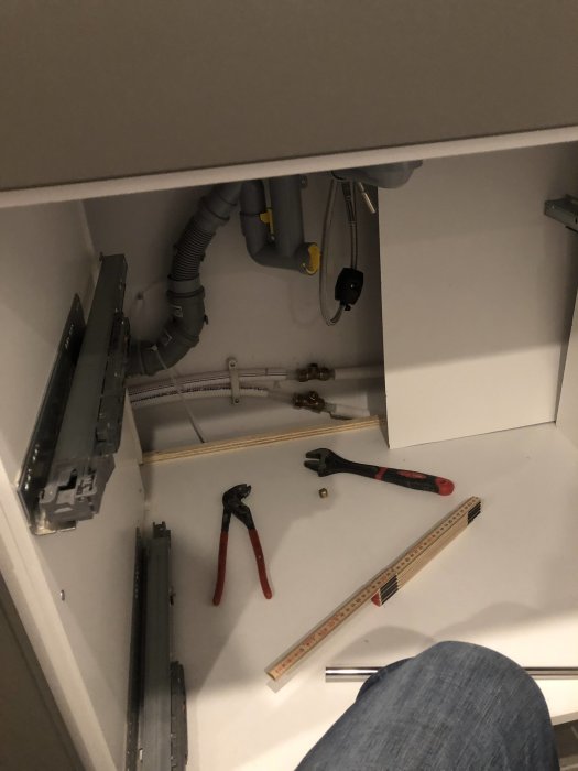 Vy inifrån skåp med rörinstallationer och verktyg för montering av kran.