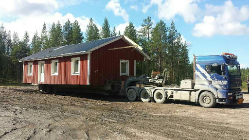 Rött fritidshus lastat på en blå lastbil redo för avhämtning.