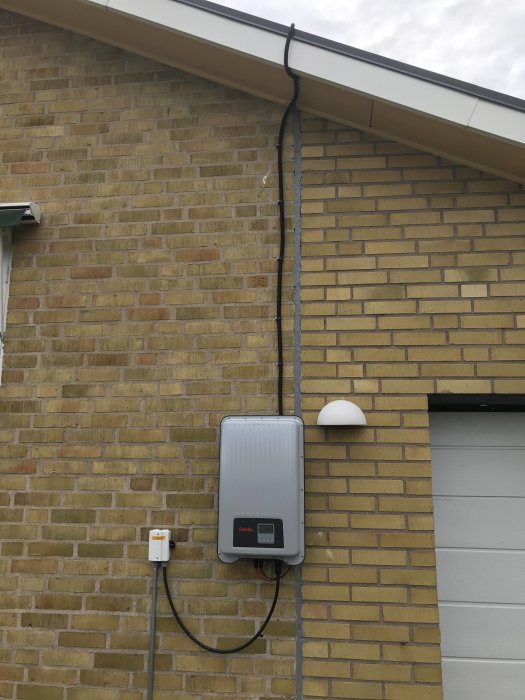 Solpanelers kabel dragen oorganiserat längs en tegelvägg ned till en inverter på husets fasad.