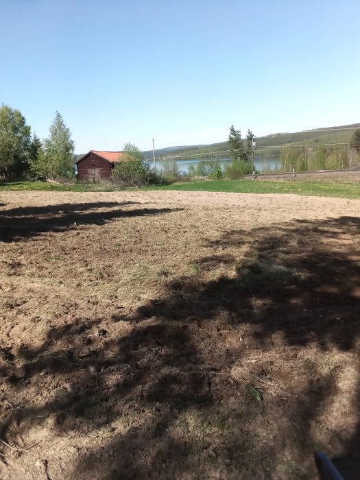 Stort odlingsland som ska harvas, med stuga och sjö i bakgrunden.