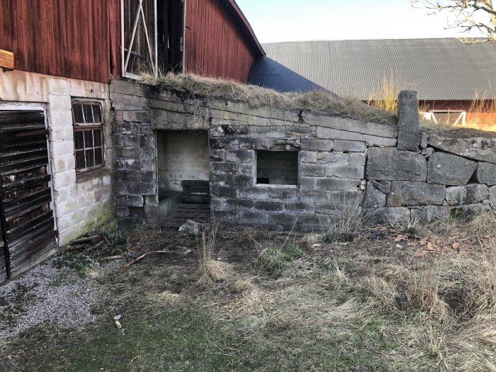 Förfallen vägg på en loge med delvis murade sektioner och skadade områden nära ett gammalt fönster och dörröppning.