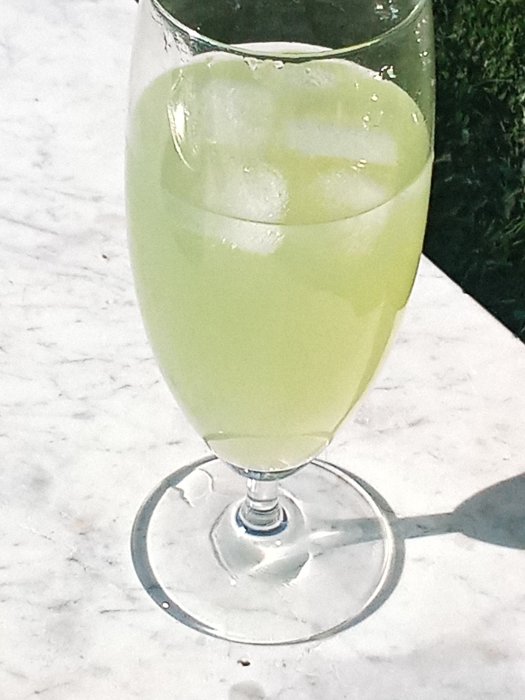 Ett glas med den ljusgula drinken "ljusnan sunset" med isbitar, på en marmorbänk.