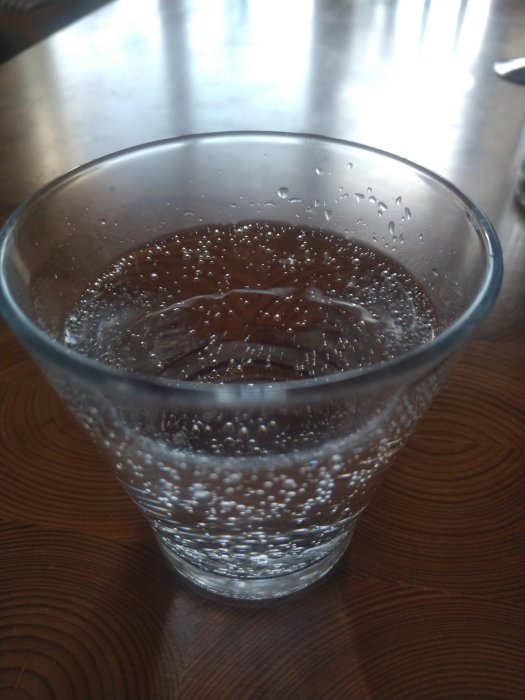 Ett glas med kolsyrat vatten på ett bord, bubblor syns tydligt genom glaset.