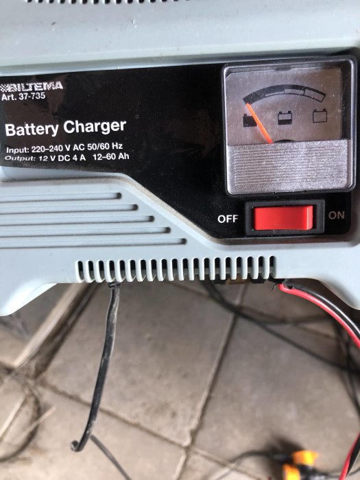 Batteriladdare med mätare som visar full laddning och strömbrytare i "ON" läge.