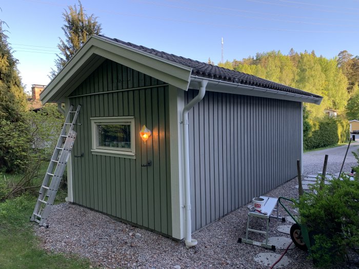 Nymålad garagebyggnad i demidekk ultimate skiffergrå med vita detaljer, en stege lutad mot väggen.