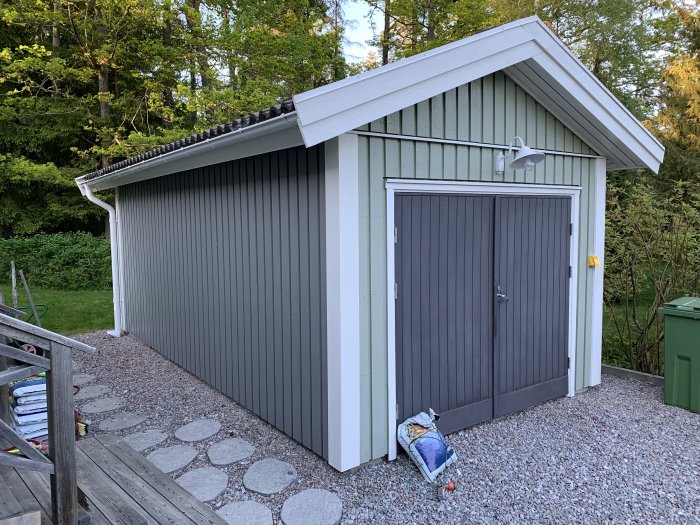 Ett nymålat garage med skiffergrå fasad och vita hörndetaljer, med en grusgång leder upp till de dubbla dörrarna.