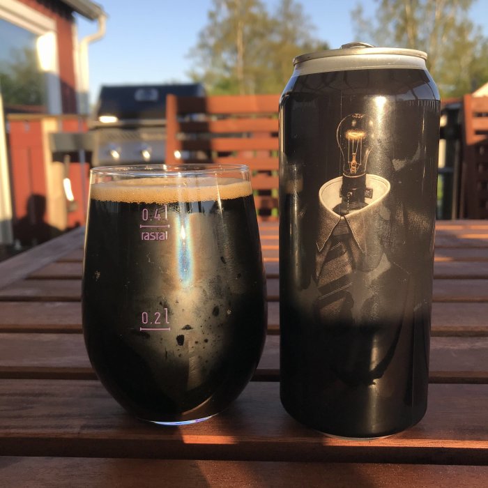 Ett glas fyllt med mörk porter på ett träbord bredvid en ölburk med lampmotiv i solnedgången.