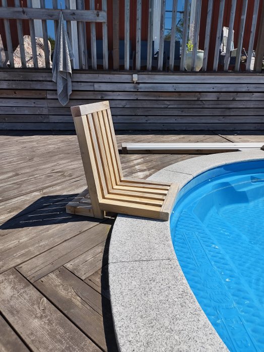 Hemmagjord trästol designad för att sitta vid poolkanten på en träterrass i solljus.