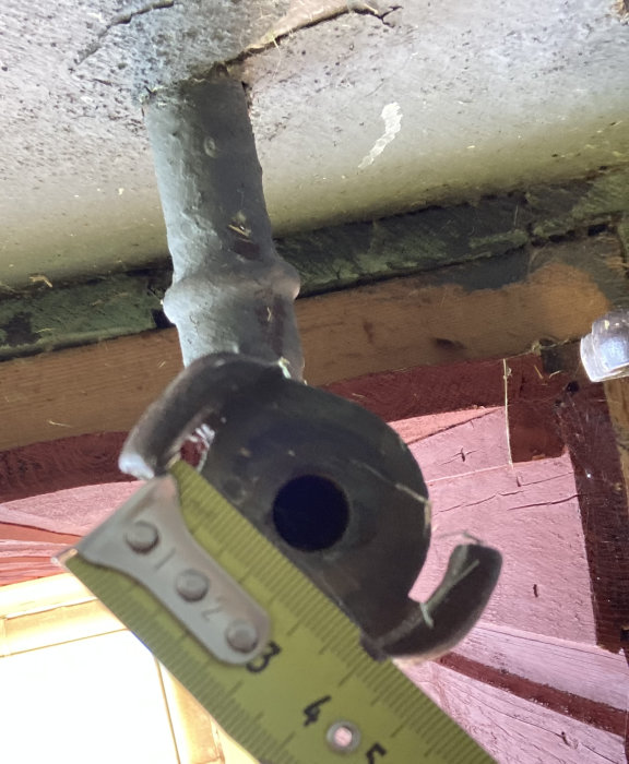 Gammal trädgårdskran liknande en brandslangskoppling mäts med tumstock mot en träbakgrund.