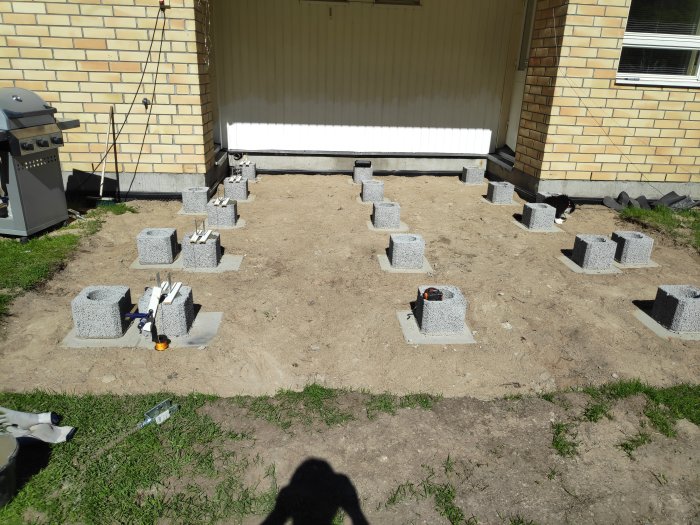 Grundplintar i rad för byggprojekt, murblock och gjutna betongplattor, verktyg och byggmaterial synliga.