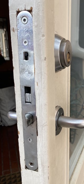 Närbild på ett Assa-lås i en vit dörrkarm med en mätsticka som visar dörrtjockleken.
