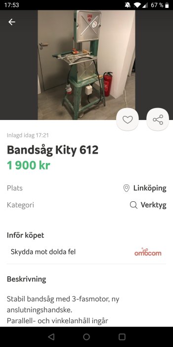 Grön och grå bandsåg, modell Kity 612, på en trälåda i ett rum, bredvid en brandsläckare, med tillbehör på arbetsbordet.