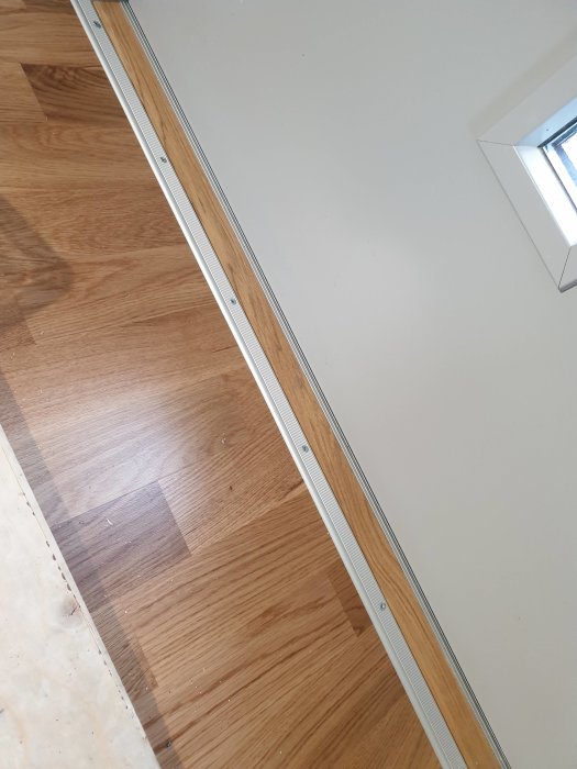 Nyinstallerad dörrtröskel mellan laminatgolv och betonggolv i rum.