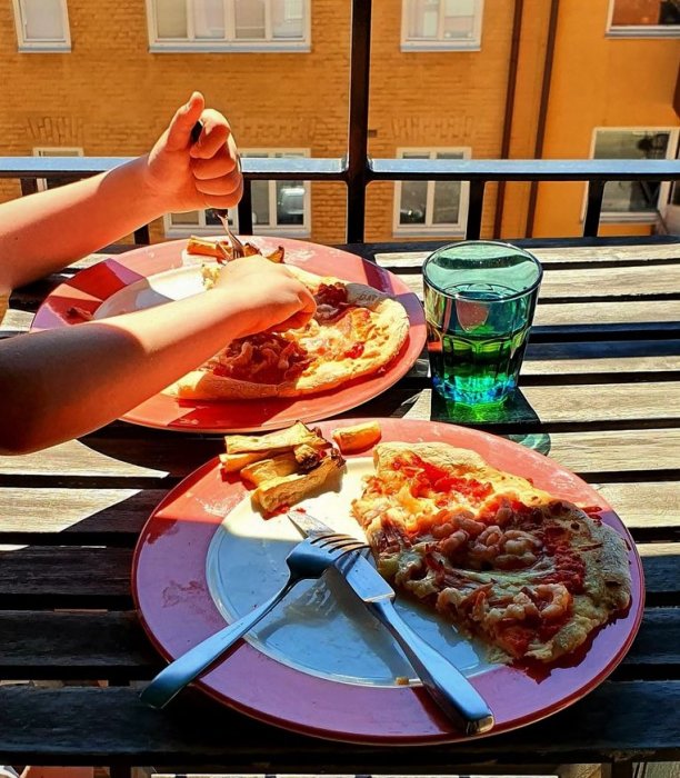 Person som äter hembakad pizza på balkong med soligt väder.