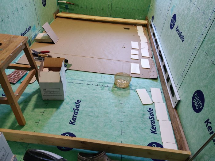 Förberedelse för kakelsättning i rum med synliga mätmarkeringar, verktyg och utspridda vita plattor.