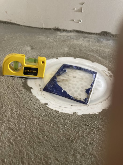 Golvbrunn inspäcklad i betong snett med våg vid sidan för att visa nivån.