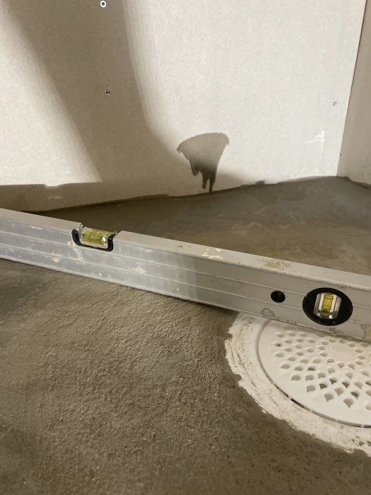 Vattenpass ligger på betonggolv vilket visar lutning mot en golvbrunn.