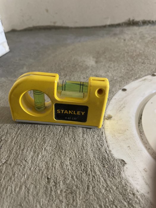 Gul Stanley vattenpass kontrollerar ytas planhet nära vit flens på ett skarvat betonggolv.