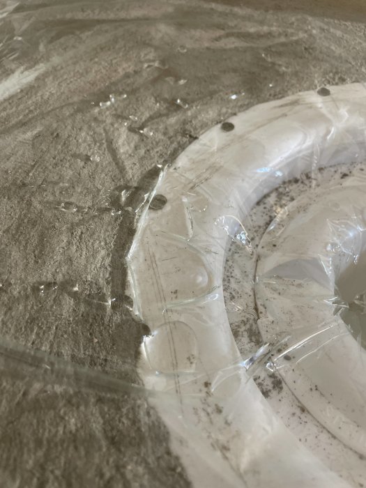 Vattenansamling på kanten av en betongyta med plastöverdrag frågar om behovet att spackla för jämnhet.