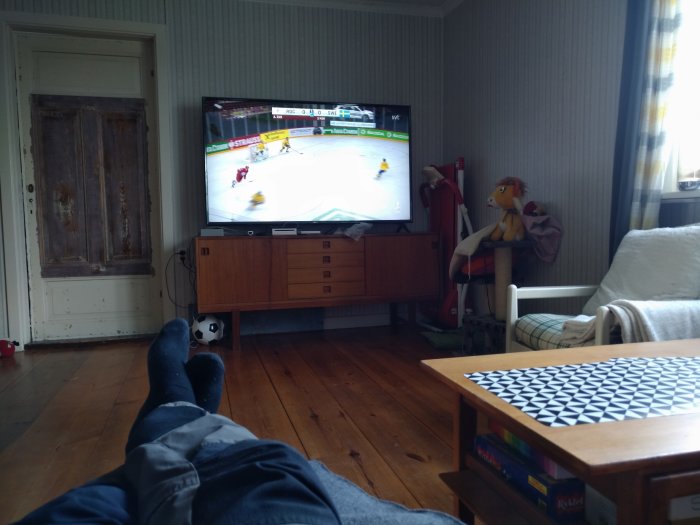 Person med fötterna upp, tittar på ishockeymatch på TV i ett vardagsrum.