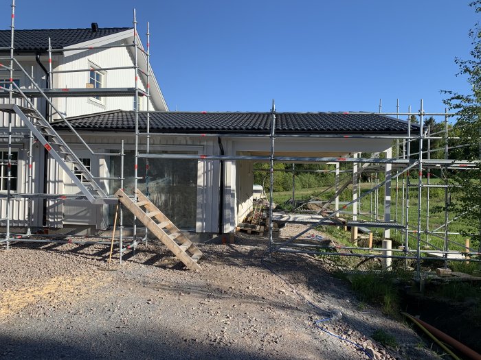 Ny målad carport på ett hus med byggnadsställningar och soligt väder.