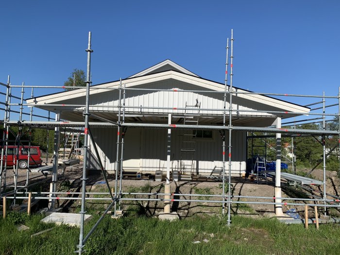 Ny målning på en carport som omges av byggnadsställningar under klarblå himmel.