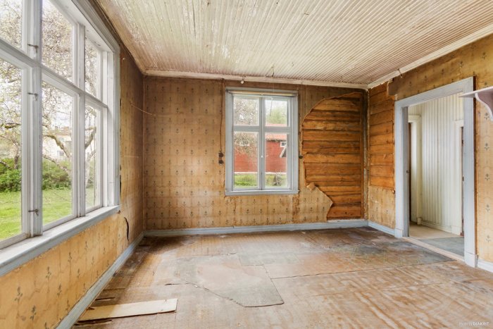 Skadat rum i gammalt hus med fuktmärken och trasiga väggar, behöver omfattande renovering.